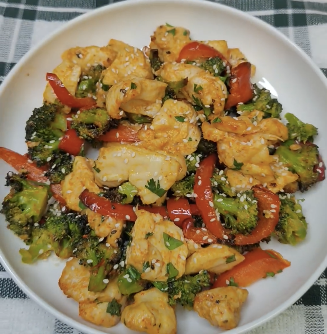 Air fryer chicken and broccoli bowl with red bell pepper, sesame seeds and green garnish in a white bowl